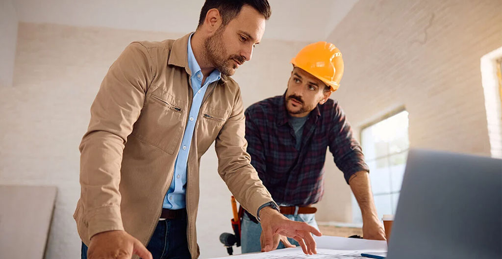 Professionnel du bâtiment présentant un plan de rénovation à un couple de propriétaires dans un bureau d'agence contemporain